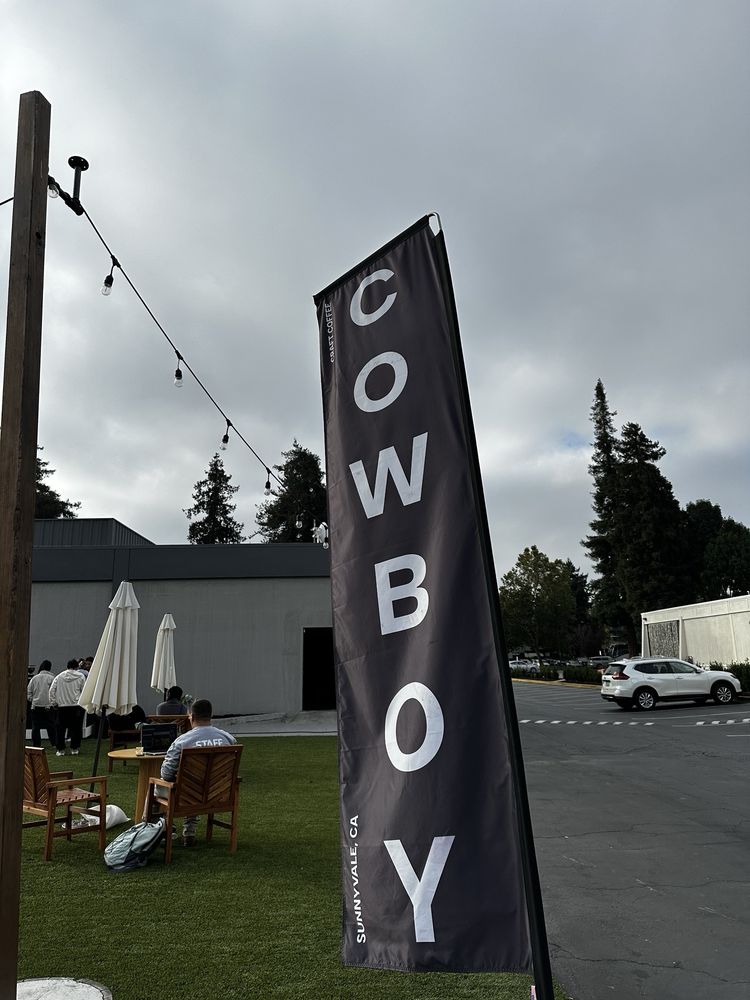 Cowboy Coffee crowd gathered under white umbrellas with string lights and blue sky